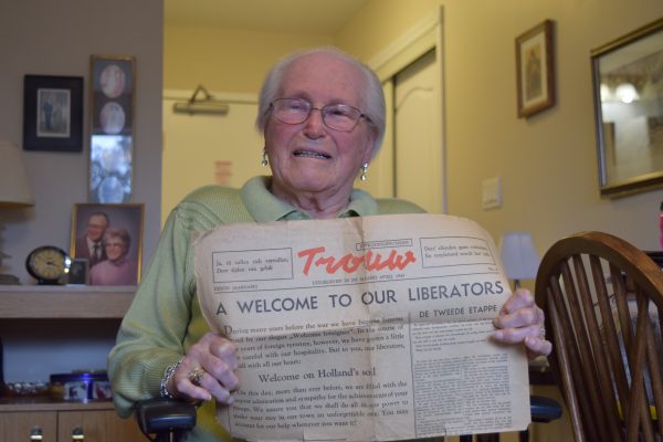 An elderly lady holds up a Dutch newspaper with a headline in English that reads: "A Welcome to our Liberators".