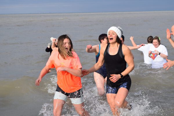 Two girls hurriedly run out of Lake Ontario while laughing,
