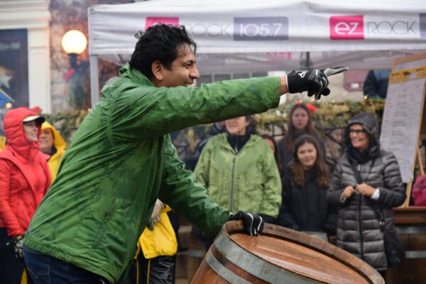 A man smileswhile pointing away from the camera and resting his other hand on the top of a wine barrel.