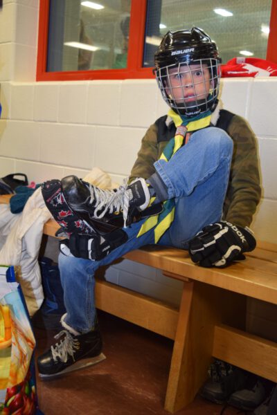 A beaver scout lace up his skates looks into the picture with a startled look on his face.