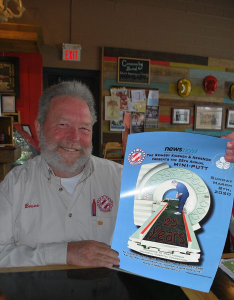A man smiles while holding a poster detailing the upcoming kinsmen mini-putt tournament.