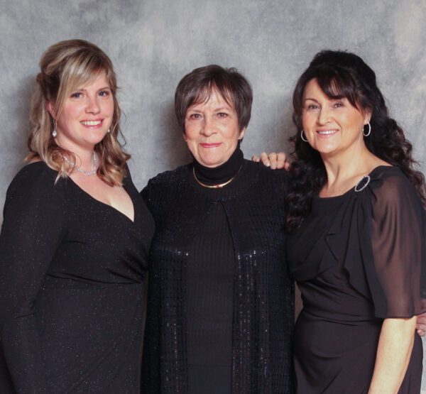 Three ladies in black dresses pose together while smiling.