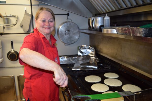 A woman smiles while flipping pancakes on a grill.