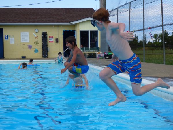 Three kids jump into an outdoor pool.