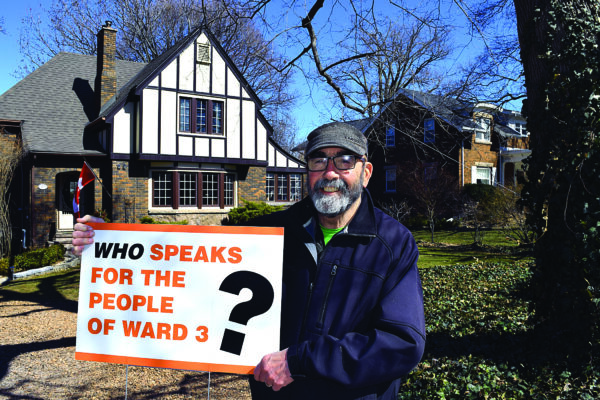 A with glasses and a beard holds up a sign that reads: "who speaks for the people of ward 3?"
